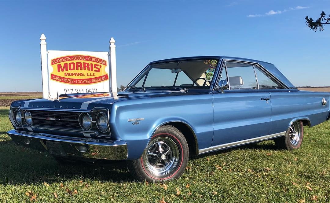 restored blue two-door plymouth with white detailing parked in front of Morris' Mopars, LLC sign